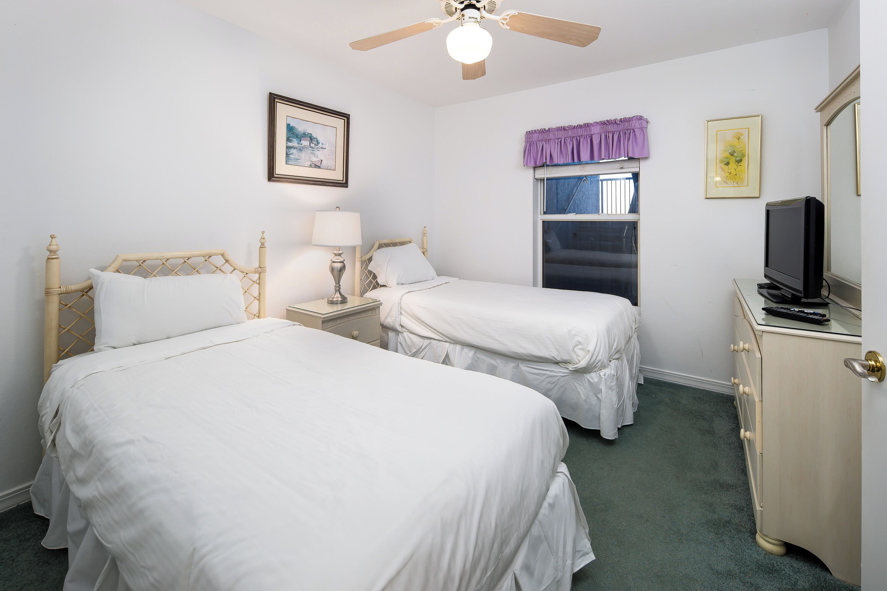 A hotel room with two beds, a ceiling fan, a TV, a dresser, and a window with a purple curtain.