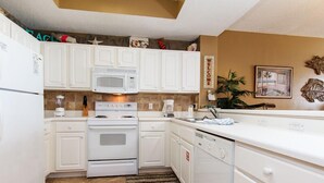 Cocina compacta con muebles blancos, microondas, estufa y lavavajillas. Se ve un cartel que dice 'WELCOME'.