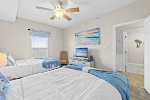 A bedroom with two beds, a ceiling fan, a TV, and a painting of a beach scene. - Gulf Dunes 508 - The Golden Nautilus (Fort Walton Beach)