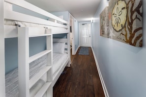 A hallway with bunk beds, a door, and a wall with a painting. - Pelican Isle 311 - Oceans Embrace (Fort Walton Beach)