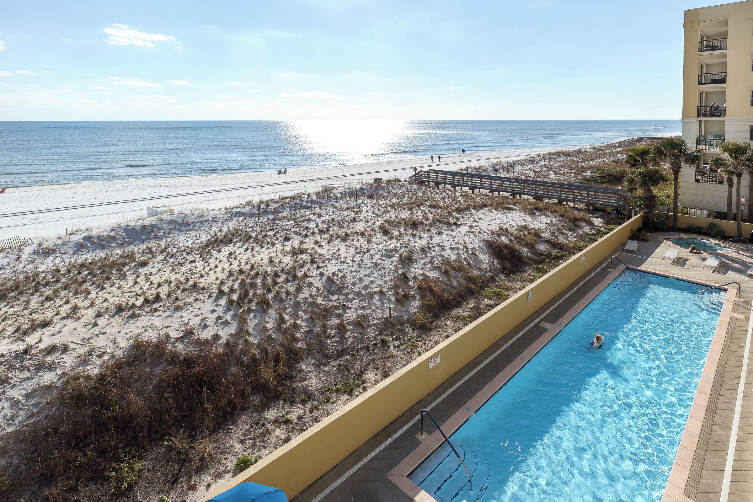 Une piscine située à côté d’une plage, avec une promenade en bois menant au rivage.