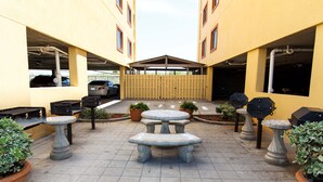 Un patio al aire libre con mesas de piedra y parrillas de barbacoa, rodeado de edificios amarillos.