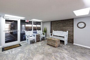 A reception area with a white bench, a wooden coffee table, and a clock on the wall. - Gulf Dunes 416 - Ocean's Edge (Fort Walton Beach)
