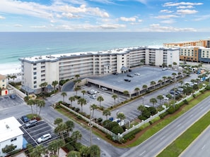 Ein mehrstöckiges Hotel mit Parkplatz, neben einem Strand und mit Blick aufs Meer.