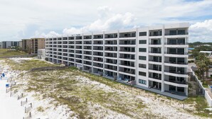 Un hotel moderno con diversi piani e balconi, affacciato su una spiaggia con un paesaggio sabbioso e un cielo sereno.