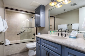 Une salle de bain moderne avec une douche à parois de verre, des toilettes, un lavabo avec trois robinets et un grand miroir.
