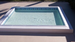 Una piscina rettangolare con bordo bianco e interno azzurro, circondata da un solarium in cemento e un basso siepe.