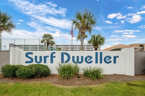 Señal de Surf Dweller, con cielo despejado y palmeras al fondo.