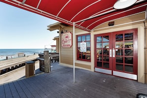 Una terraza de madera con toldo rojo, un letrero que dice 'The Crab Trap Seafood and Oyster Bar' y vista al océano.