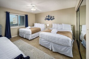 A hotel room with two beds, a ceiling fan, a window with curtains, a wall-mounted anchor decoration, and a mirror. - Surf Dweller 502 - The Dune Retreat (Fort Walton Beach)