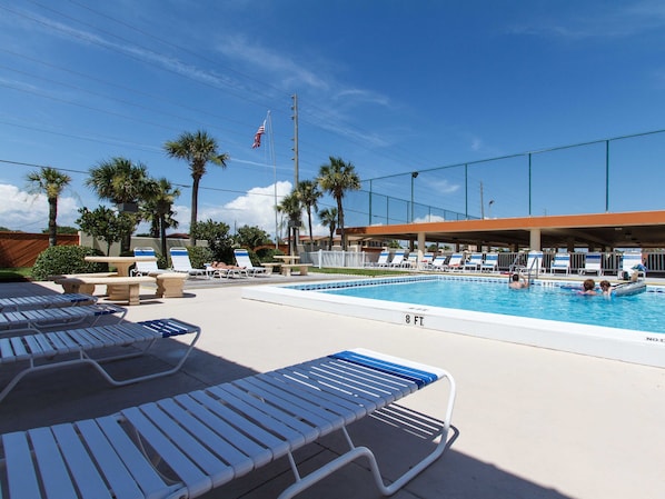 A swimming pool with lounge chairs, palm trees, and a flag. - Surf Dweller 502 - The Dune Retreat (Fort Walton Beach)