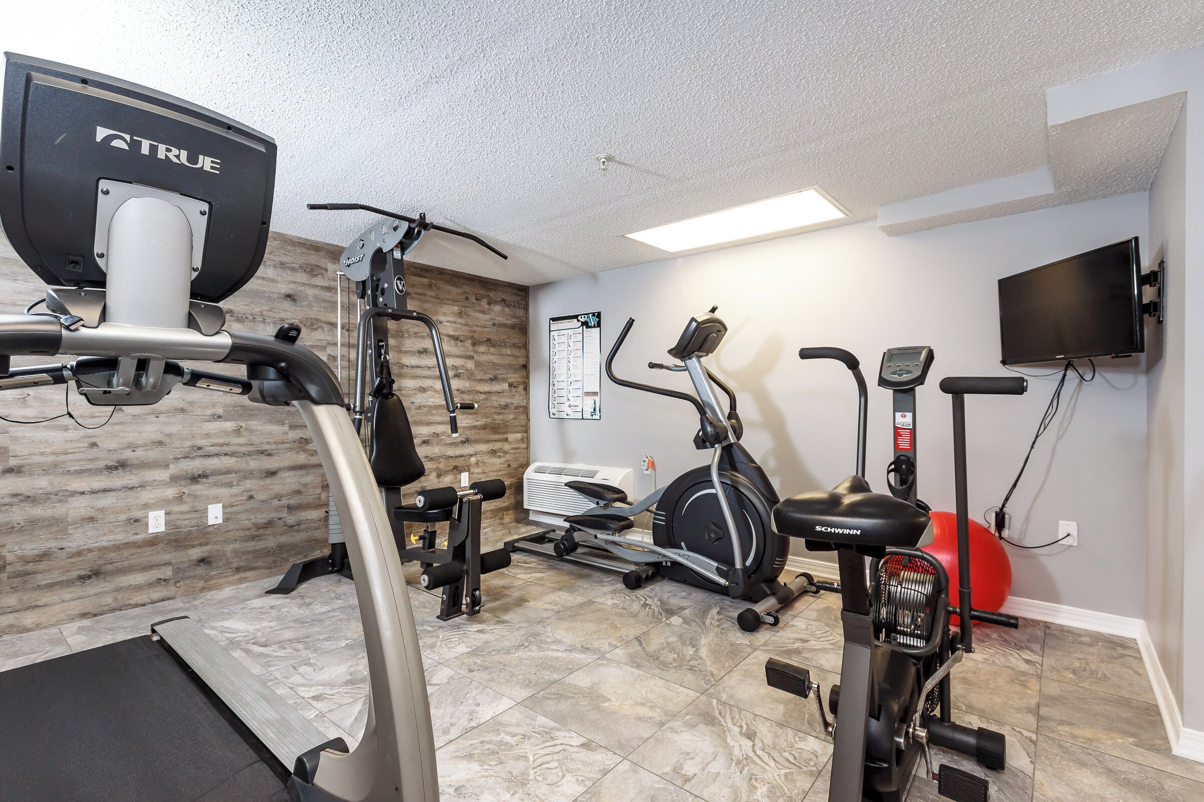 A home gym with various exercise equipment including a treadmill, stationary bike, and elliptical machine.