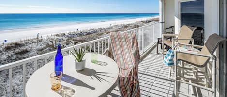 A balcony with a view of the beach, a round table with a bottle and glass, and two chairs.