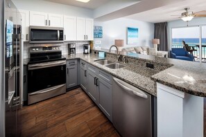 A modern kitchen with stainless steel appliances, granite countertops, and a view of the ocean through the balcony. - Pelican Isle 510 - Sunset Serenade (Fort Walton Beach)