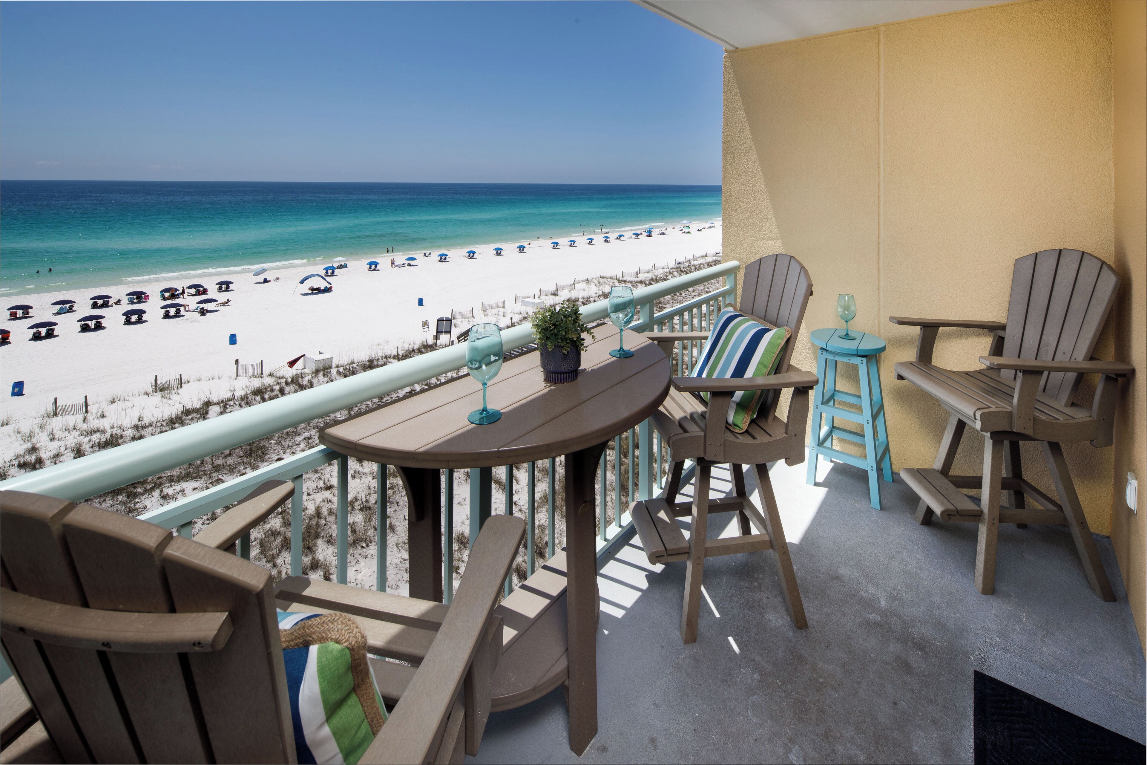 A balcony with a view of a beach, wooden furniture, and a small table with a glass.