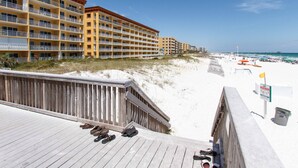 A beachfront hotel with multiple balconies, a sandy beach, and a wooden boardwalk with shoes. - Gulf Dunes 301 - Seas the Day (Fort Walton Beach)