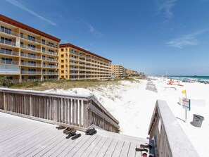 Ein Strandhotel mit mehreren Balkonen, einem Sandstrand und einer Holzpromenade mit Schuhen.