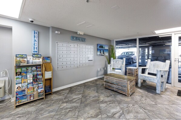 A reception area with a bulletin board, a desk, a chair, and a view of the parking area. - Gulf Dunes 207 - Blue Skies & Beach Vibes (Fort Walton Beach)