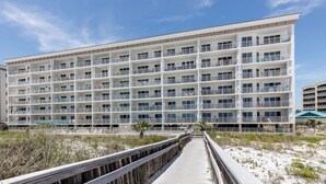 A multi-story hotel with balconies, a boardwalk leading to the beach, and a sandy landscape. - Gulf Dunes 315 - Salt and Serenity (Fort Walton Beach)
