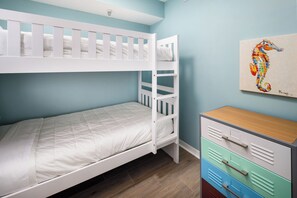 A bunk bed with a white frame and a lower bed with a white mattress. There is a wooden dresser with multiple drawers and a seahorse painting on the wall. - Gulf Dunes 412 - Sunset Fiesta (Fort Walton Beach)