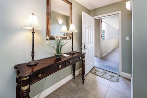 A wooden console table with lamps and a mirror, a potted plant, and a door leading to a staircase. - Summerlin 305 - Breezy Palms (Fort Walton Beach)