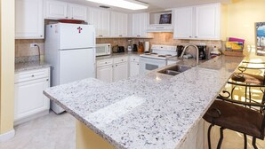 A kitchen with white cabinets, a granite countertop, a refrigerator, a microwave, a stove, and a sink. - Islander 3004 - Coral Dreams (Fort Walton Beach)