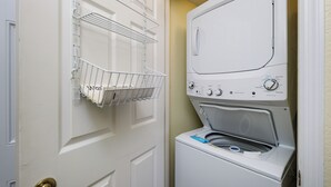 A laundry room with a front-loading washer and dryer, a metal drying rack, and a door with a brass doorknob. - Islander 3004 - Coral Dreams (Fort Walton Beach)