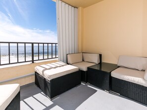 Een balkon met uitzicht op het strand, een bank, een kleine tafel en een stoel.