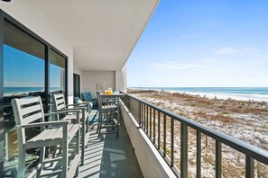Un balcon avec vue sur la plage, comprenant une table avec des chaises et une petite lampe de table.