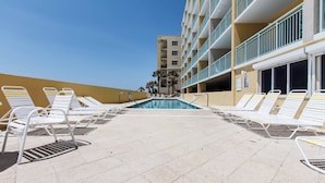 Zona de piscina con sillones blancos y cielo azul despejado.