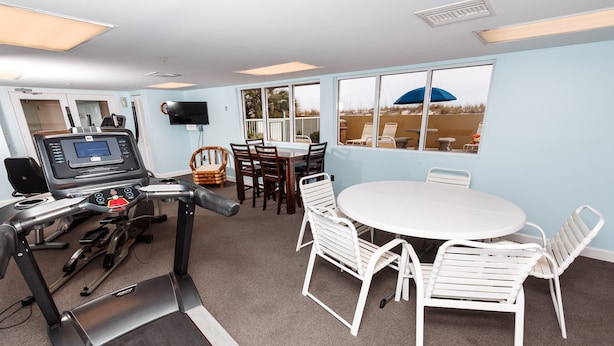 Una habitación con cinta de correr, una mesa de comedor con sillas y un ventanal con vista a la playa.