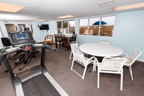 Una habitación con cinta de correr, una mesa de comedor con sillas y un ventanal con vista a la playa.