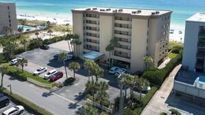 Um hotel com vários andares e estacionamento, localizado ao lado de uma praia com guarda-sóis e piscina.