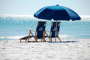 Due sedie da spiaggia sotto un ombrellone blu su una spiaggia sabbiosa, con l'oceano sullo sfondo.
