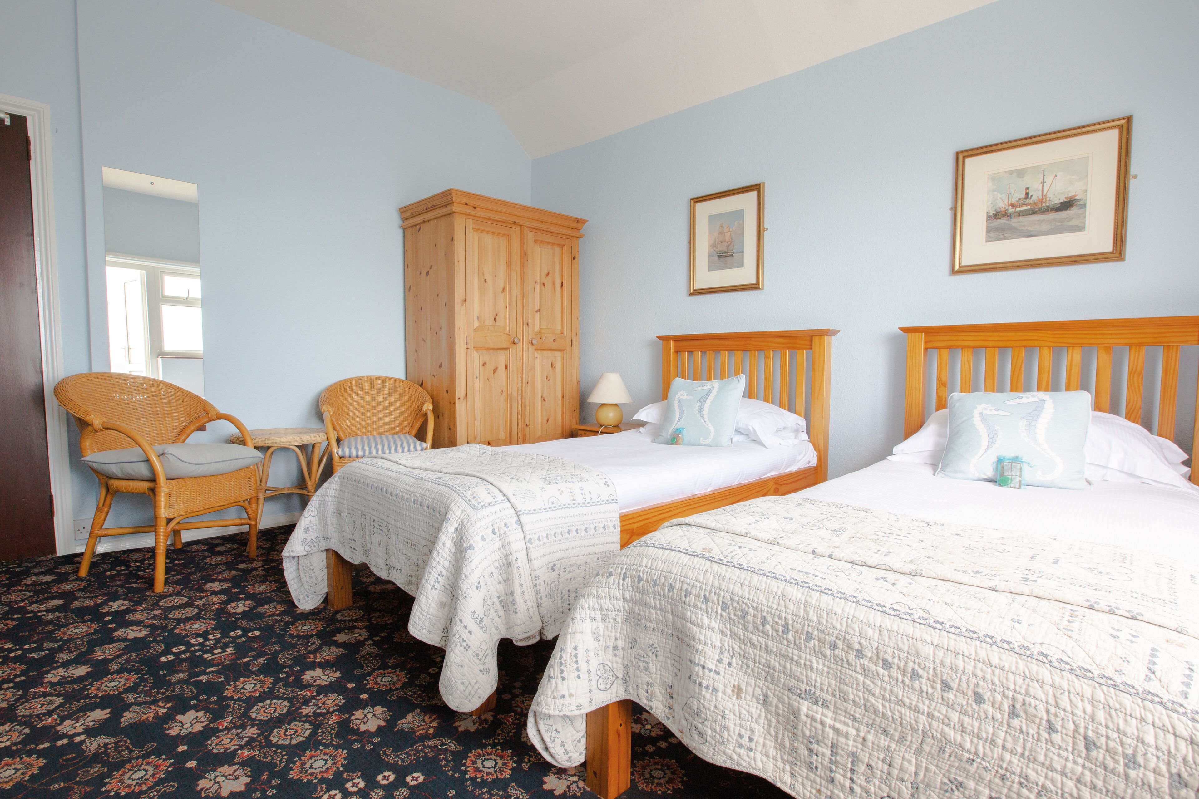 A bedroom with two single beds, a wooden wardrobe, a chair, and a small table.
