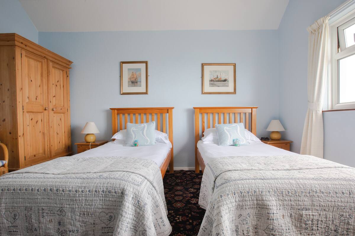 A room with two beds, wooden headboards, a large wardrobe, and framed pictures on the wall.
