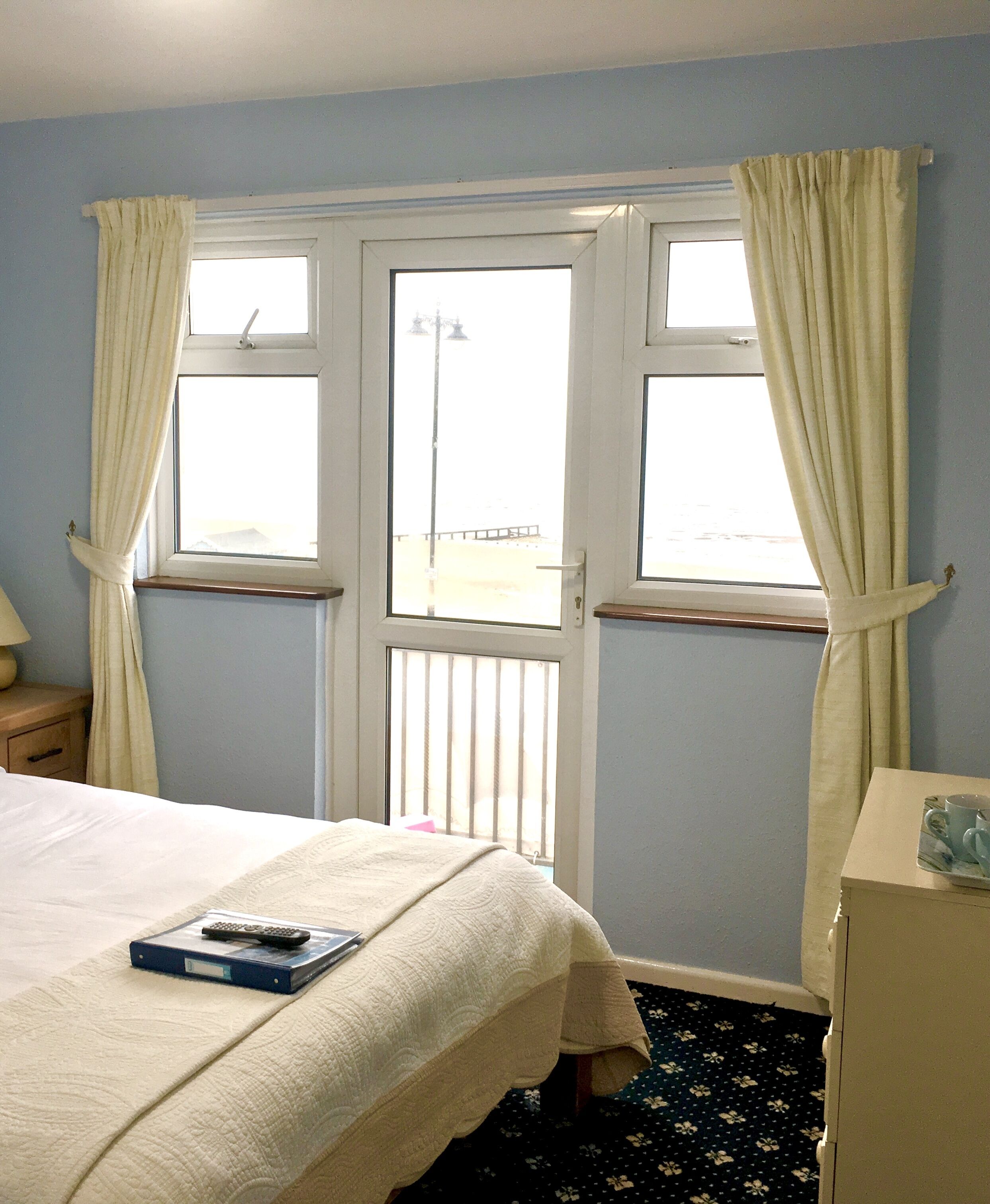 A hotel room with a bed, a bedside table, a dresser, and a window with curtains.