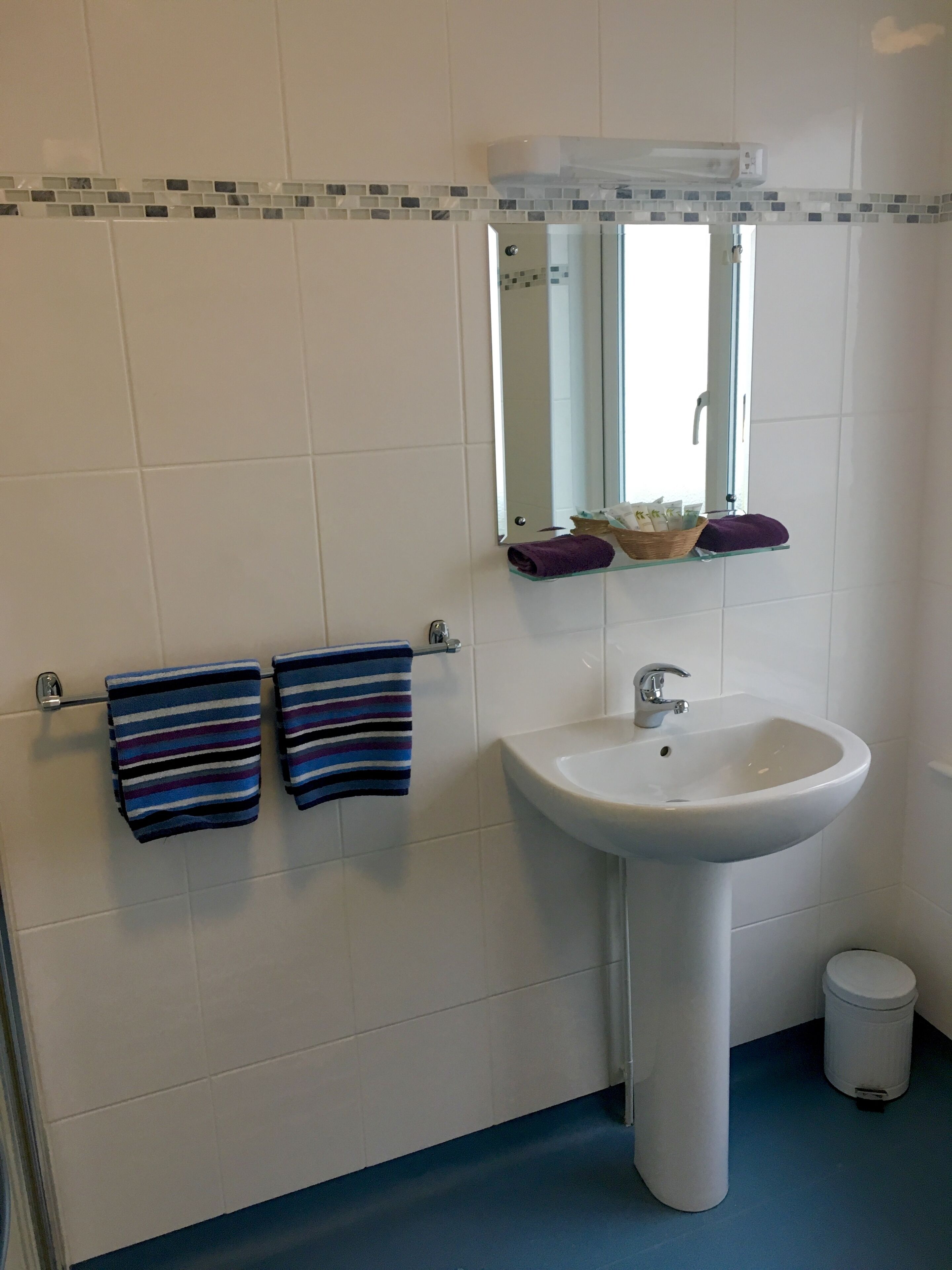 A bathroom with a white sink, a mirror above it, and two striped towels hanging on a rack.