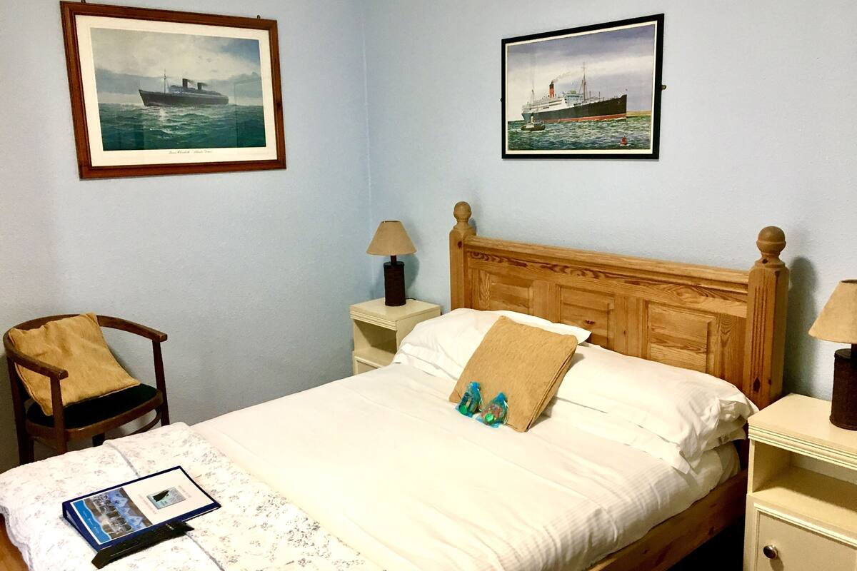 A neatly made bed with a wooden headboard, a chair with a cushion, two bedside tables with lamps, and two framed pictures on the wall.