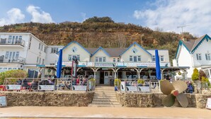 A seaside hotel with multiple dining areas, a prominent staircase leading to the entrance, and a view of the surrounding cliffs.