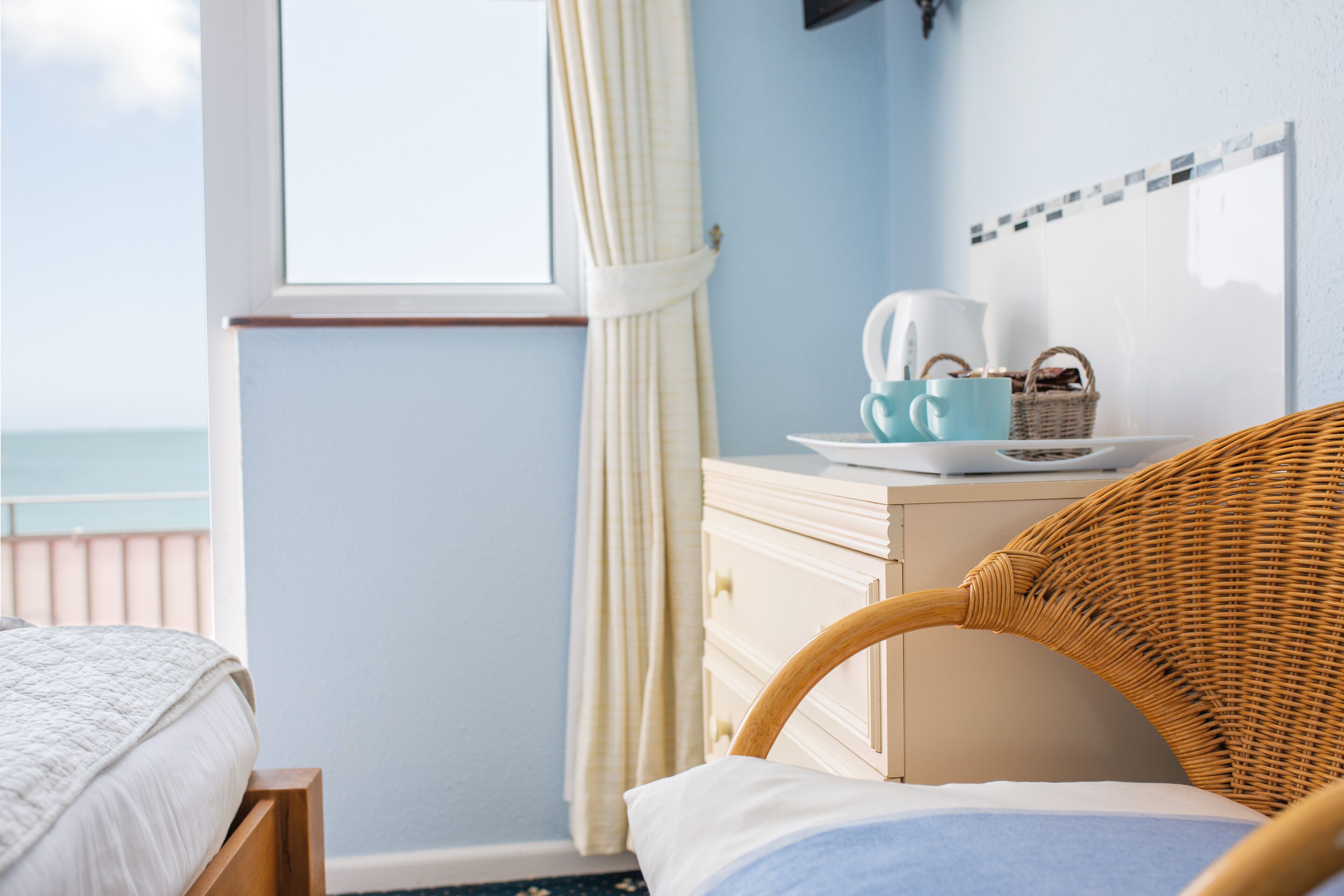 A bedroom with a bed, a wicker chair, a dresser, and a window with curtains.