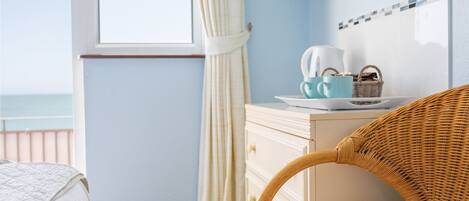 A bedroom with a bed, a wicker chair, a dresser, and a window with curtains.