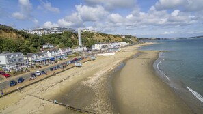 A coastal town with a sandy beach, a promenade with shops and cafes, and buildings along the hillside.