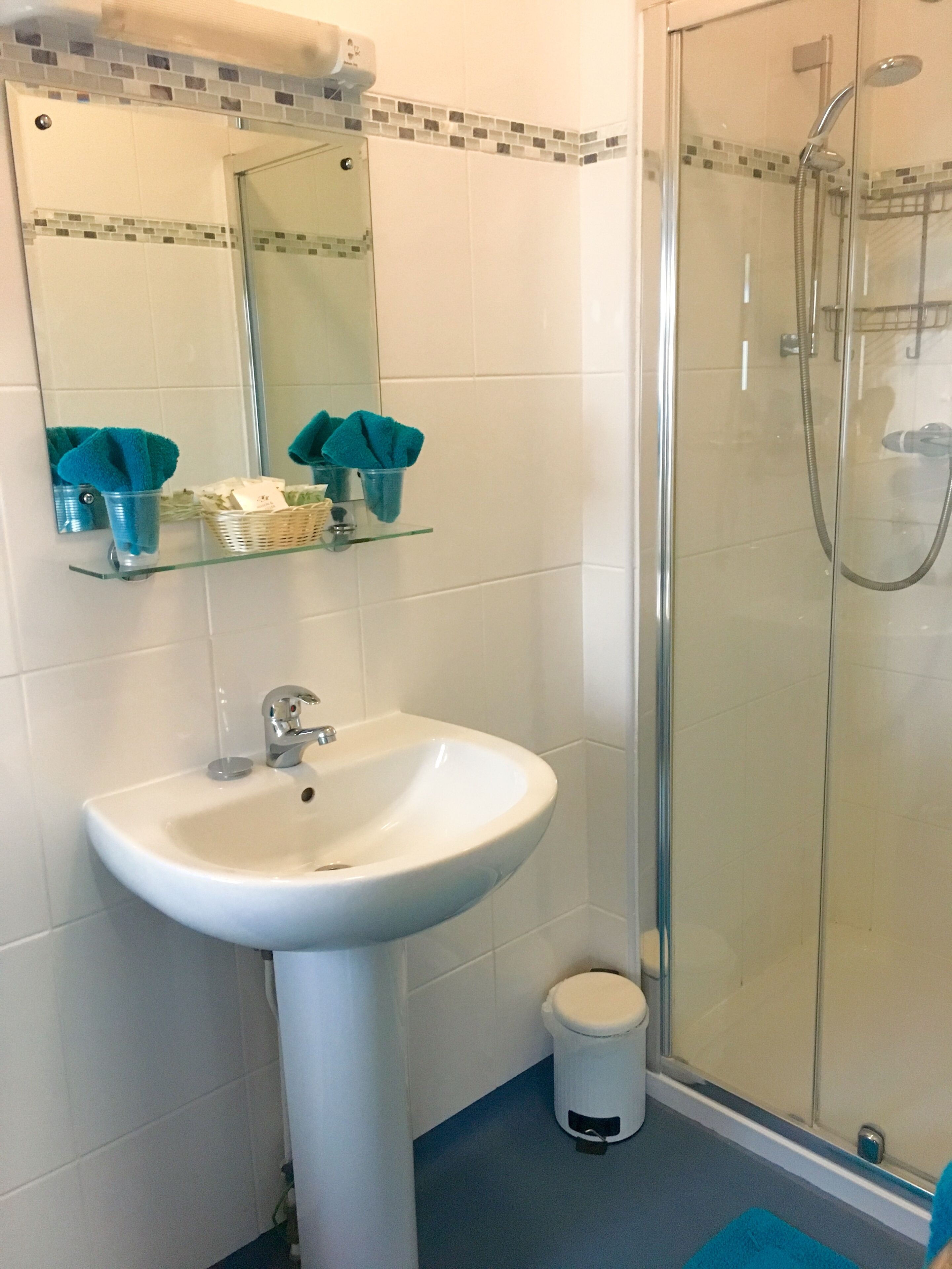 Une salle de bain avec un lavabo blanc, une cabine de douche en verre et un miroir bordé de mosaïques.