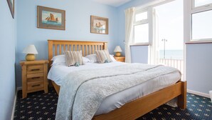 A bedroom with a wooden bed, two bedside tables, a window with curtains, and two framed pictures on the wall.