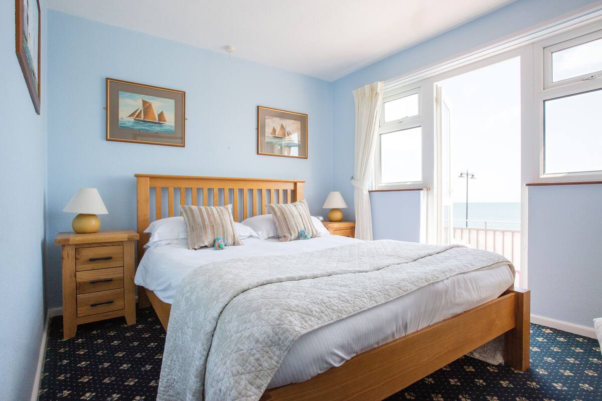 A bedroom with a wooden bed, two bedside tables, a window with curtains, and two framed pictures on the wall.