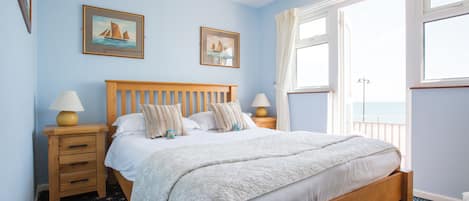 Une chambre à coucher avec un lit en bois, deux tables de chevet, une fenêtre avec des rideaux et deux tableaux encadrés accrochés au mur.