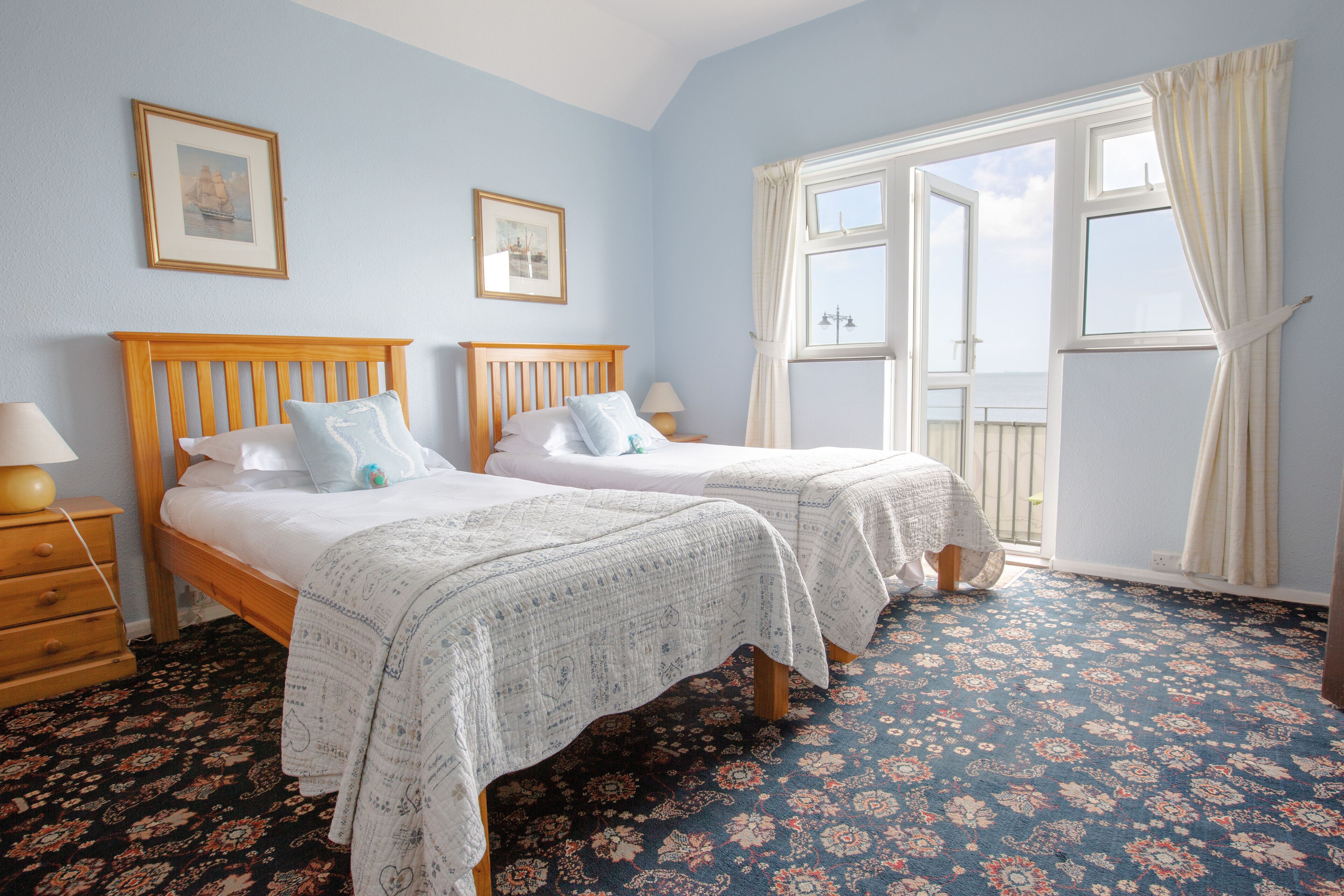 A bedroom with two beds, a wooden headboard, a patterned carpet, and a window with curtains.
