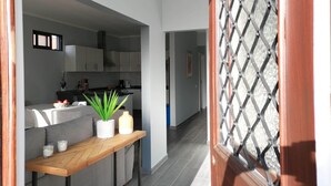 A modern kitchen with grey cabinets, a wooden table with a plant, and a view into the dining area.