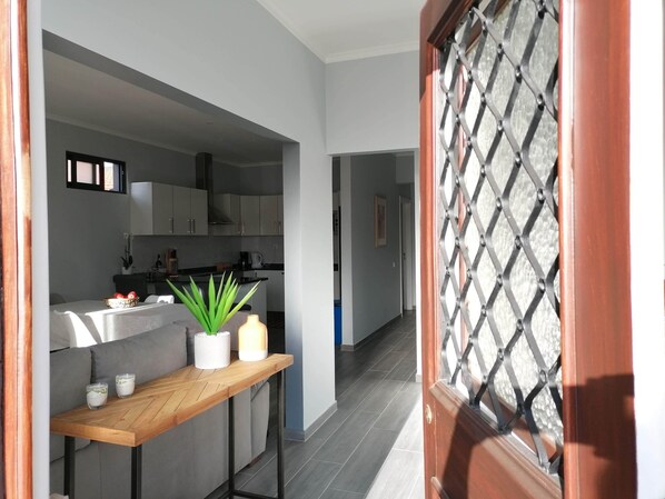 A modern kitchen with grey cabinets, a wooden table with a plant, and a view into the dining area.